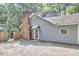 Home exterior showcasing gray siding, red brick chimney and door with mature landscaping and paved patio at 2334 Dawn Trl, Durham, NC 27712