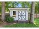 Charming backyard shed with gray trim, surrounded by mature trees and a lush lawn at 907 Stuart Dr, Mebane, NC 27302
