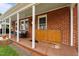 Cozy front porch with a porch swing, white columns, and brick siding at 9964 N Chestnut St, Middlesex, NC 27557