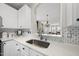 A kitchen sink with white cabinets, mosaic backsplash, and a view to the living room at 4413 Sugarbend Way, Raleigh, NC 27606