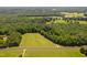 Aerial view of a grassy field surrounded by lush trees, with a road running through the property at 1909 Ira Rd, Efland, NC 27243