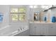Sunlit bathroom featuring a jetted tub under a window, double sinks, and a serene, all-white color palette at 92 Summer Dawn, Pittsboro, NC 27312