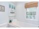 Bright bathroom with a tub, window with blind, and decorative shelving at 1405 Pennsylvania Ave, Durham, NC 27705