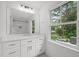 Bright bathroom showcasing a large mirror, white cabinets, and a window with a view of the outdoors at 2551 Drake Ave, Durham, NC 27705