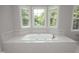 Bathroom featuring a whirlpool tub with tile surround, double windows, and gold fixtures at 4217 Grahamstone Rd, Raleigh, NC 27610