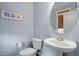Well-lit half bath featuring a pedestal sink, round mirror, and blue painted walls at 5712 Turner Store Ln, Raleigh, NC 27603
