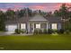 Charming single-story home boasts an attached two-car garage, a manicured lawn and inviting front porch at sunset at 244 Lasswade Ct, Zebulon, NC 27597