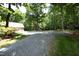 Overview of the property featuring mature trees and a gravel driveway with multiple structures at 5464 Bass Mountain Rd, Snow Camp, NC 27349