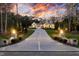 Stately home with a long driveway, lush landscaping, and exterior lamp posts illuminating the property at 387 Riverstone Dr, Pittsboro, NC 27312