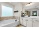 Bright bathroom featuring a soaking tub with tiled surround and a double vanity with white cabinetry at 1154 Yorkshire Dr, Burlington, NC 27215