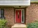 Bright red front door with glass panels and brick surround, nestled amongst lush green shrubbery at 204 Chatterson Dr, Raleigh, NC 27615