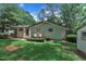 An exterior view of a cottage-style home featuring a spacious backyard with a grassy lawn and natural landscaping at 3205 Dell Dr, Raleigh, NC 27609