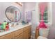 This bathroom features a round mirror, wood cabinets, and a window with pink curtains at 713 Saint Catherines Dr, Wake Forest, NC 27587