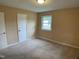 Tan-carpeted bedroom featuring neutral walls, a window letting in natural light, and a simple overhead light at 2915 Ross Rd, Durham, NC 27703