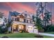 Elegant two-story home with a stone and siding facade, a welcoming front porch, and a three-car garage at sunset at 4104 Green Chase Way, Apex, NC 27539