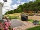 View of the outdoor stone patio with black metal table set, grill, and beautiful landscaping at 4179 Dunkirk Dr, Burlington, NC 27215