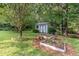 Backyard garden shed surrounded by a garden, landscaping, and mature trees at 457 Poplar Forest Ln, Pittsboro, NC 27312