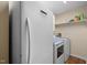 Bright laundry room featuring a white washer, dryer, refrigerator, and storage shelves at 110 Starlite Dr, Carrboro, NC 27510