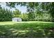 Lush backyard with a greenhouse surrounded by mature trees and green grass at 1146 W Holt St, Mebane, NC 27302