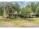 Charming home featuring a light yellow exterior, green metal roof, spacious porch, and lush landscaping with mature trees at 6200 Us-401 S, Bunnlevel, NC 28323