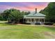Charming home featuring a light yellow exterior, green metal roof, spacious porch, and lush landscaping with a stunning sunset backdrop at 6200 Us-401 S, Bunnlevel, NC 28323