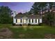 Charming white home with black shutters, a cozy front porch, and landscaped lawn beneath a beautiful sunset sky at 107 Winter Ct, Selma, NC 27576