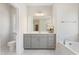 Well-lit bathroom featuring a grey vanity, large mirror, bathtub, and marble tile at 713 Ramsours Mill Dr, Holly Springs, NC 27540