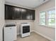Well-lit laundry room with large washer and dryer units, and dark cabinets for storage at 728 Peninsula Forest Pl, Cary, NC 27519