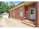 Side exterior of brick house with gray door, driveway, and a view of the detached garage at 1313 Duplin Rd, Raleigh, NC 27607