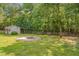 View of the spacious backyard featuring a shed, fire pit, wooden fence, and ample green space surrounded by lush trees at 300 Williamston Ridge Dr, Youngsville, NC 27596
