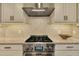 Close-up of a stainless steel gas range and range hood with a light backsplash and white cabinets at 12412 Mayhurst Pl, Raleigh, NC 27614