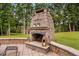 Outdoor stone fireplace on a patio with views of the lush lawn and lake at 6708 Wavcott Dr, Fuquay Varina, NC 27526