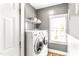 Modern laundry room with white washer and dryer, window with blinds, and upper shelving at 2218 Watersglen Dr, Apex, NC 27502