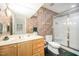 Full bathroom with a light wooden vanity, framed mirror, floral wallpaper, toilet, and shower with glass doors at 2612 Scarlet Sage Ct, Raleigh, NC 27613