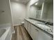 Bathroom featuring double sinks with granite countertops, white cabinetry, tub and tile floors at 116 Oakfield Trace Dr, Four Oaks, NC 27524