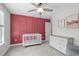 Charming bedroom with red accent wall, ceiling fan, dresser, crib, neutral color palette, and carpeted floors at 1214 Valley Dale Dr, Fuquay Varina, NC 27526