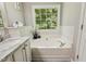 Relaxing bathtub with a large window overlooking lush greenery, complemented by marble countertops and modern fixtures at 12620 Waterlow Park Ln, Raleigh, NC 27614