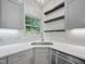 Close-up of a kitchen corner with quartz countertops, gray cabinetry, and open shelving by a window at 8640 Swarthmore Dr, Raleigh, NC 27615