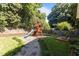Lush backyard view of the wooden playground with a slide, swing, ladder and a small deck at 1811 Ridley St, Raleigh, NC 27608