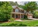 A charming brick home featuring a welcoming front porch with white columns, lush landscaping, and a well-maintained lawn at 5123 Richland Dr, Raleigh, NC 27612