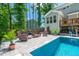 Well-manicured backyard features a pool, outdoor lounge furniture, stone patio, and a beautiful lawn surrounded by trees at 8341 Running Fern Way, Willow Springs, NC 27592