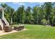 Large backyard featuring manicured lawn, mature trees, and a cozy patio with comfortable outdoor furniture at 142 Scarlet Oak Run, Clayton, NC 27520