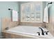A luxurious soaking tub is framed by tan tile and a large plantation shutter window in this relaxing bathroom at 142 Scarlet Oak Run, Clayton, NC 27520