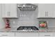 Modern cooktop with stainless steel range hood, gray backsplash and granite countertops at 265 Purple Aster St, Youngsville, NC 27596