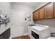 Functional laundry room with wood cabinets, white washer and dryer, and door to the side yard at 553 Lake Gaston Dr, Fuquay Varina, NC 27526