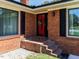Close up of brick front porch, a red front door decorated with a wreath and black shutters at 712 E Horne St, Clayton, NC 27520