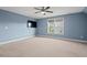 Bright bedroom featuring a ceiling fan, neutral carpet, blue walls, and a large window at 997 Windy Rd, Apex, NC 27502