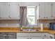 Close-up of kitchen sink area with white cabinets, butcher block countertop, neutral tile backsplash, and natural light at 6501 Battleford Dr, Raleigh, NC 27613