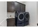 Modern laundry room with dark cabinetry, sink, and high-efficiency front-loading washer and dryer at 8420 Bells Lake Rd, Apex, NC 27539