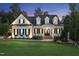 A beautiful two-story white farmhouse with black shutters, a covered porch, and manicured front lawn at dusk at 175 Stonecrest Way, Pittsboro, NC 27312
